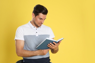 Handsome man reading book on color background, space for text