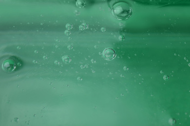 Photo of Pure transparent cosmetic gel on green background, closeup