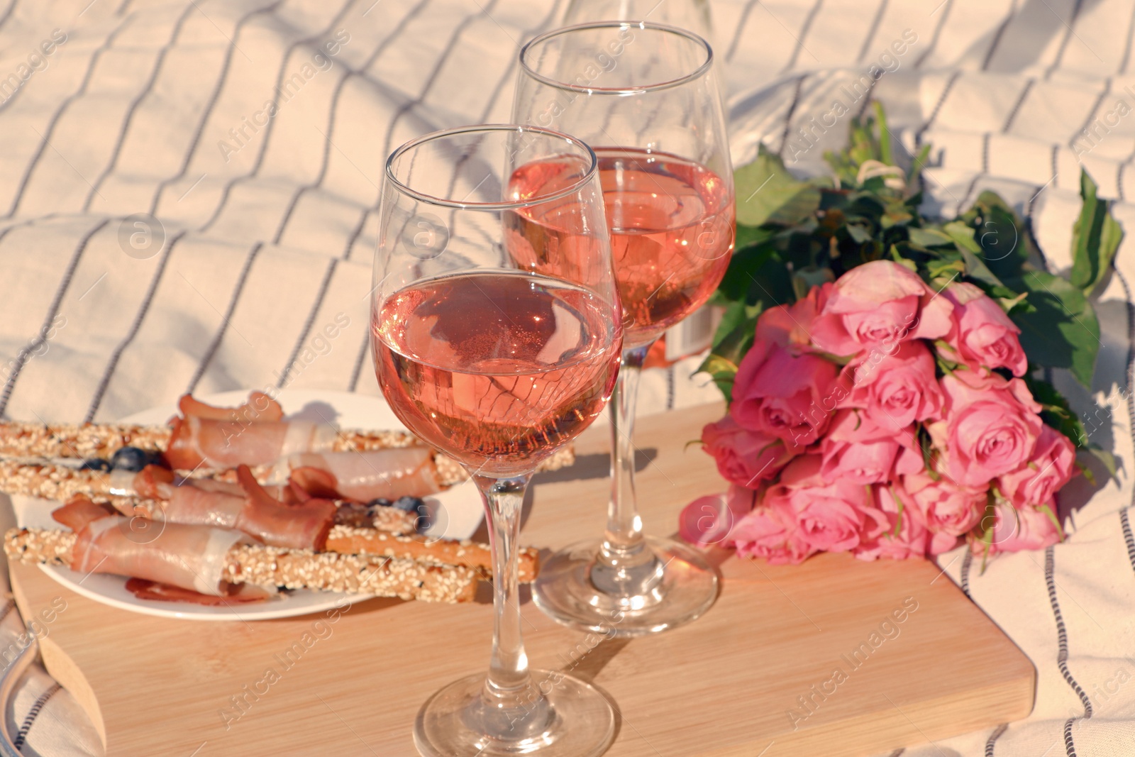 Photo of Glasses of delicious rose wine, flowers and food on white picnic blanket