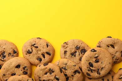 Photo of Many delicious chocolate chip cookies on yellow background, flat lay. Space for text