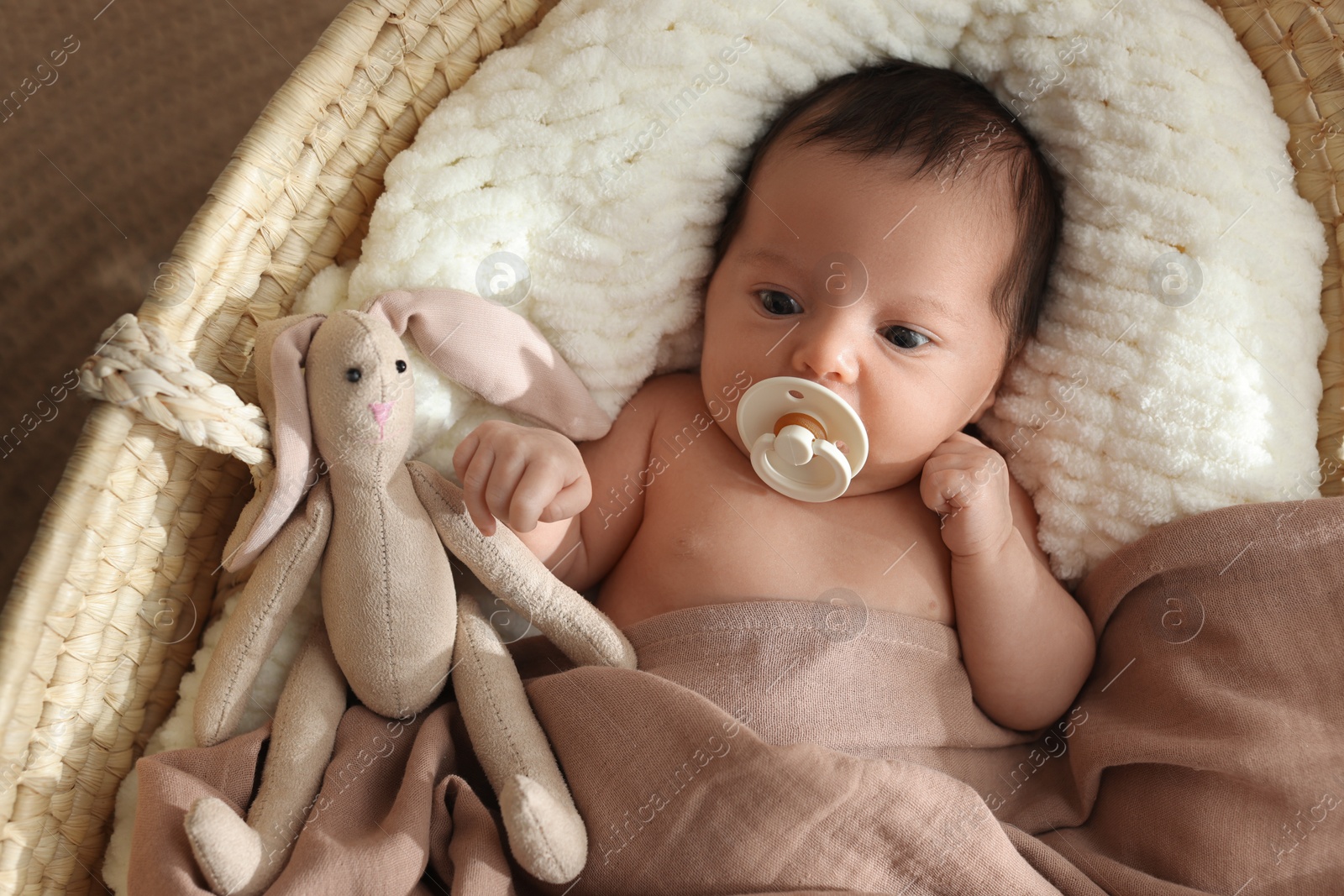 Photo of Cute newborn baby with pacifier and toy bunny lying in cradle, top view