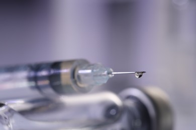 Photo of Drop of medication on syringe needle against blurred background, closeup. Space for text