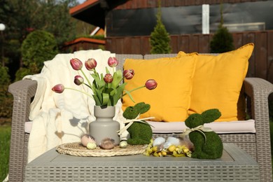 Photo of Terrace with Easter decorations. Bouquet of tulips in vase, bunny figures and decorated eggs on table outdoors