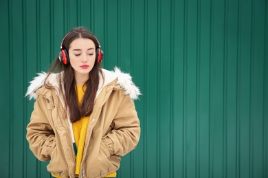 Photo of Beautiful young woman listening to music with headphones against color wall. Space for text