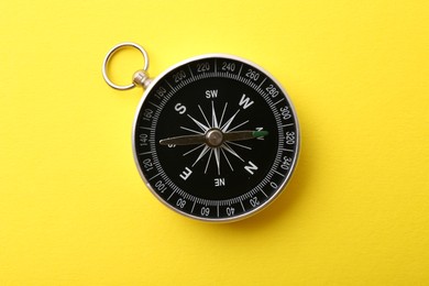 Photo of One compass on yellow background, top view. Tourist equipment