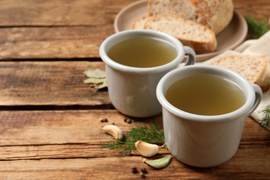 Photo of Hot delicious bouillon in cups on wooden table. Space for text