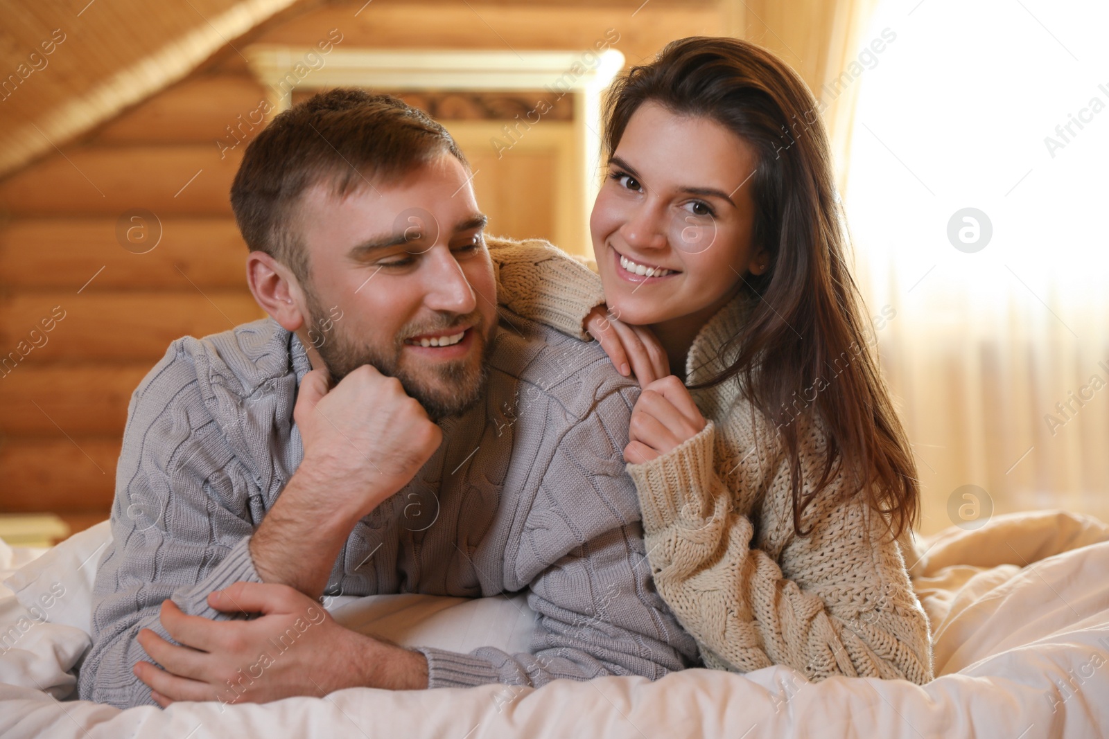 Photo of Young couple wearing warm sweaters on bed at home