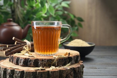 Photo of Aromatic licorice tea in cup and dried sticks of licorice root on black wooden table, space for text