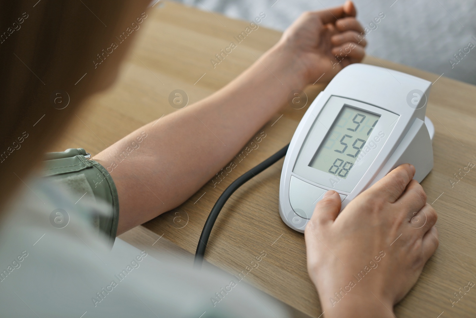 Photo of Woman checking blood pressure with sphygmomanometer at table indoors, closeup. Cardiology concept