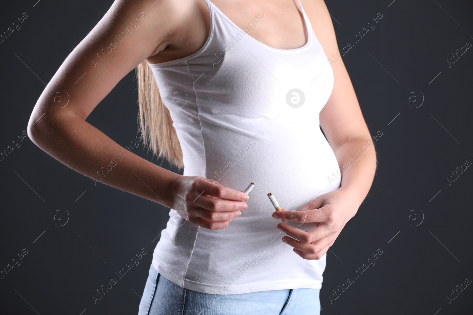 Photo of Young pregnant woman breaking cigarette on dark background, closeup. Harm to unborn baby