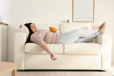 Photo of Lazy overweight woman with chips resting on sofa at home