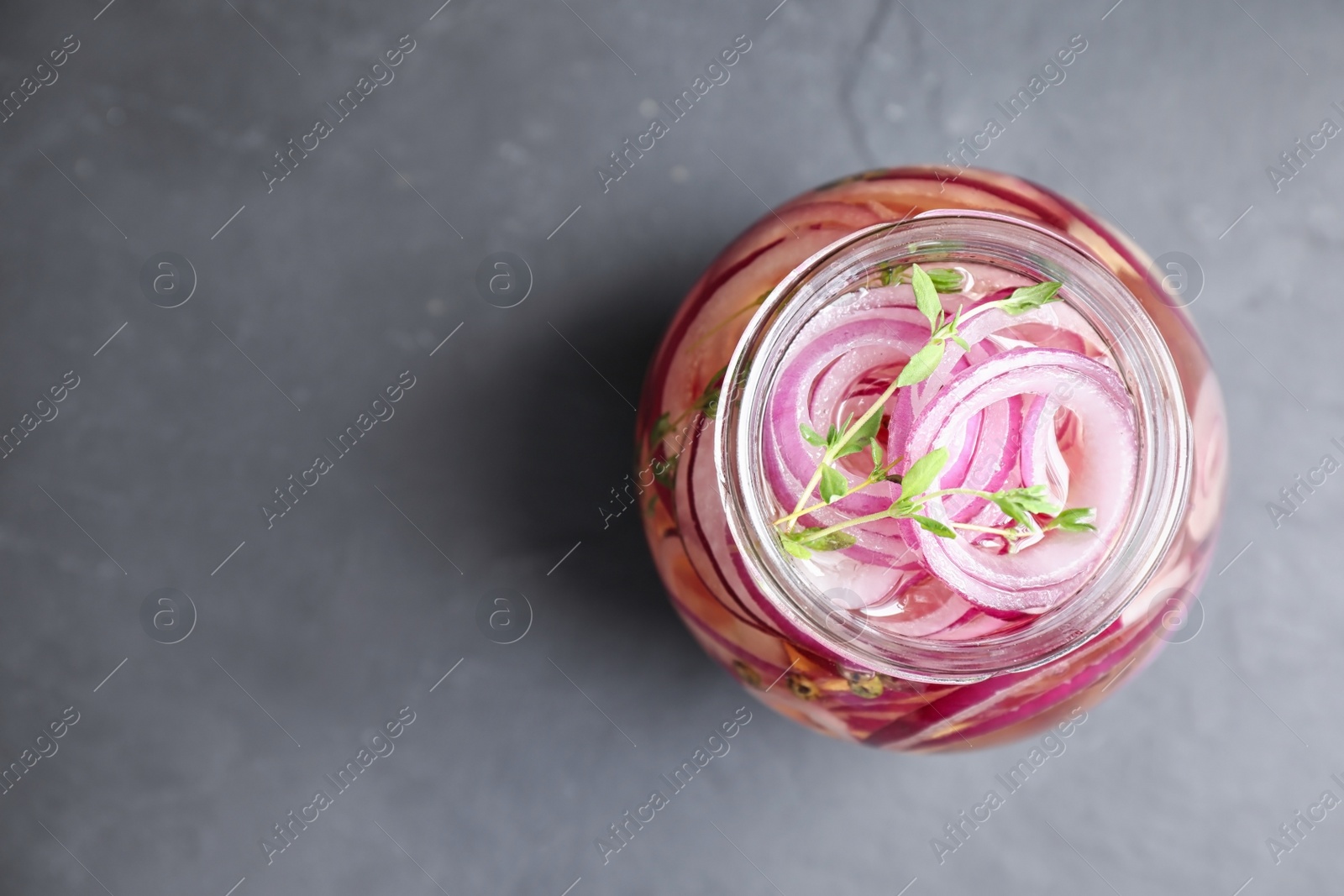 Photo of Jar of pickled onions on grey table, top view. Space for text