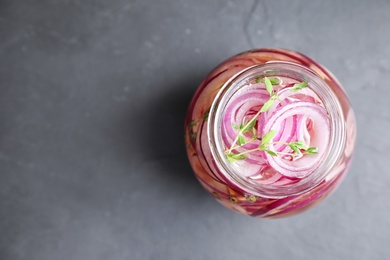 Photo of Jar of pickled onions on grey table, top view. Space for text