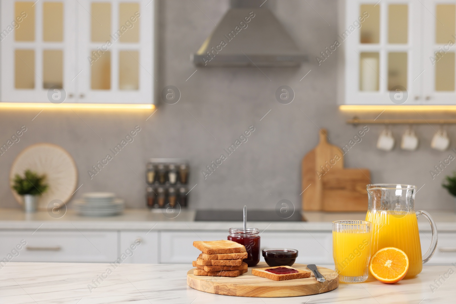 Photo of Breakfast served in kitchen. Crunchy toasts, jam and orange fresh on white table. Space for text