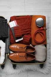 Open suitcase with folded clothes, accessories and shoes on floor, top view