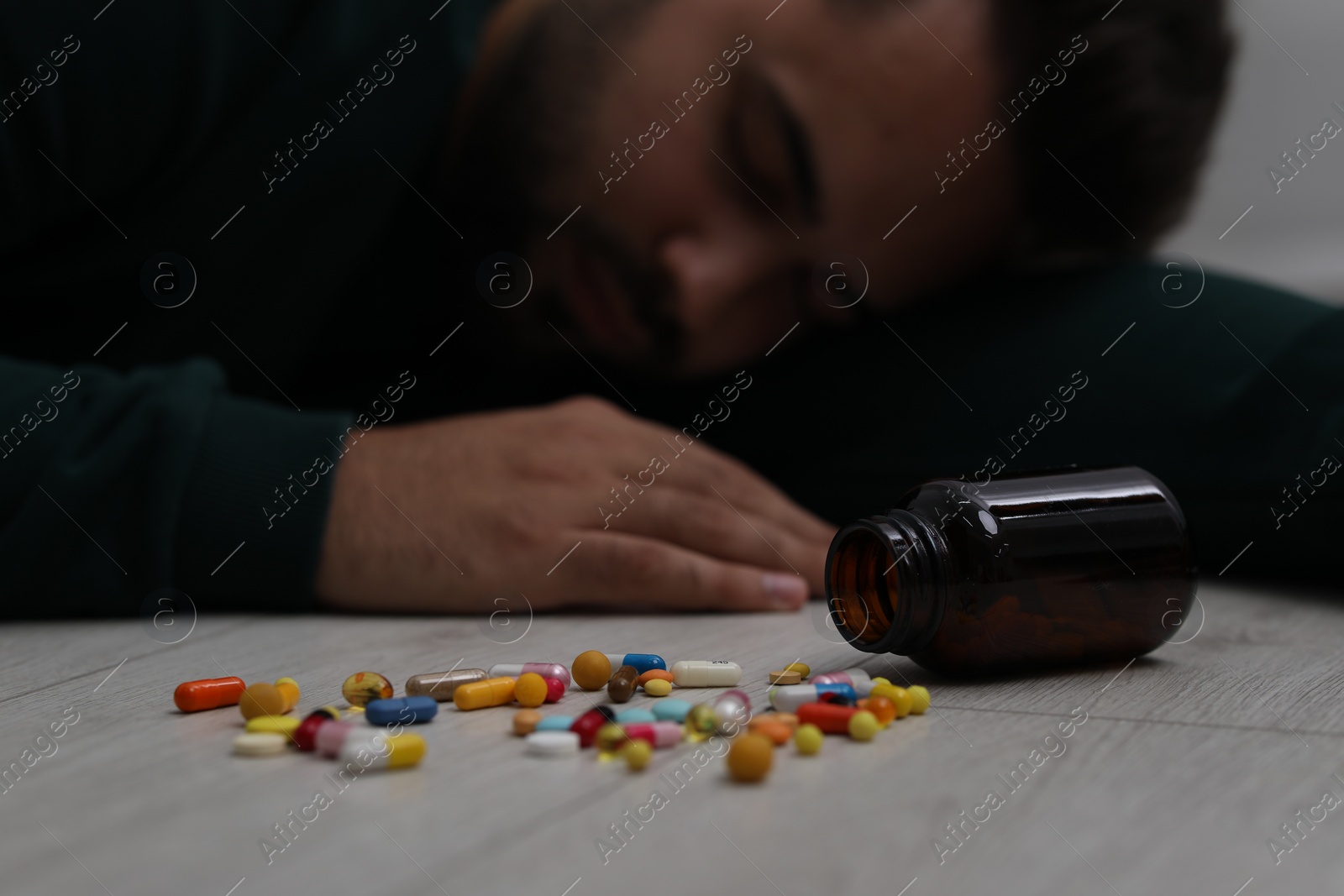 Photo of Man sleeping on floor, focus on overturned bottle with antidepressants