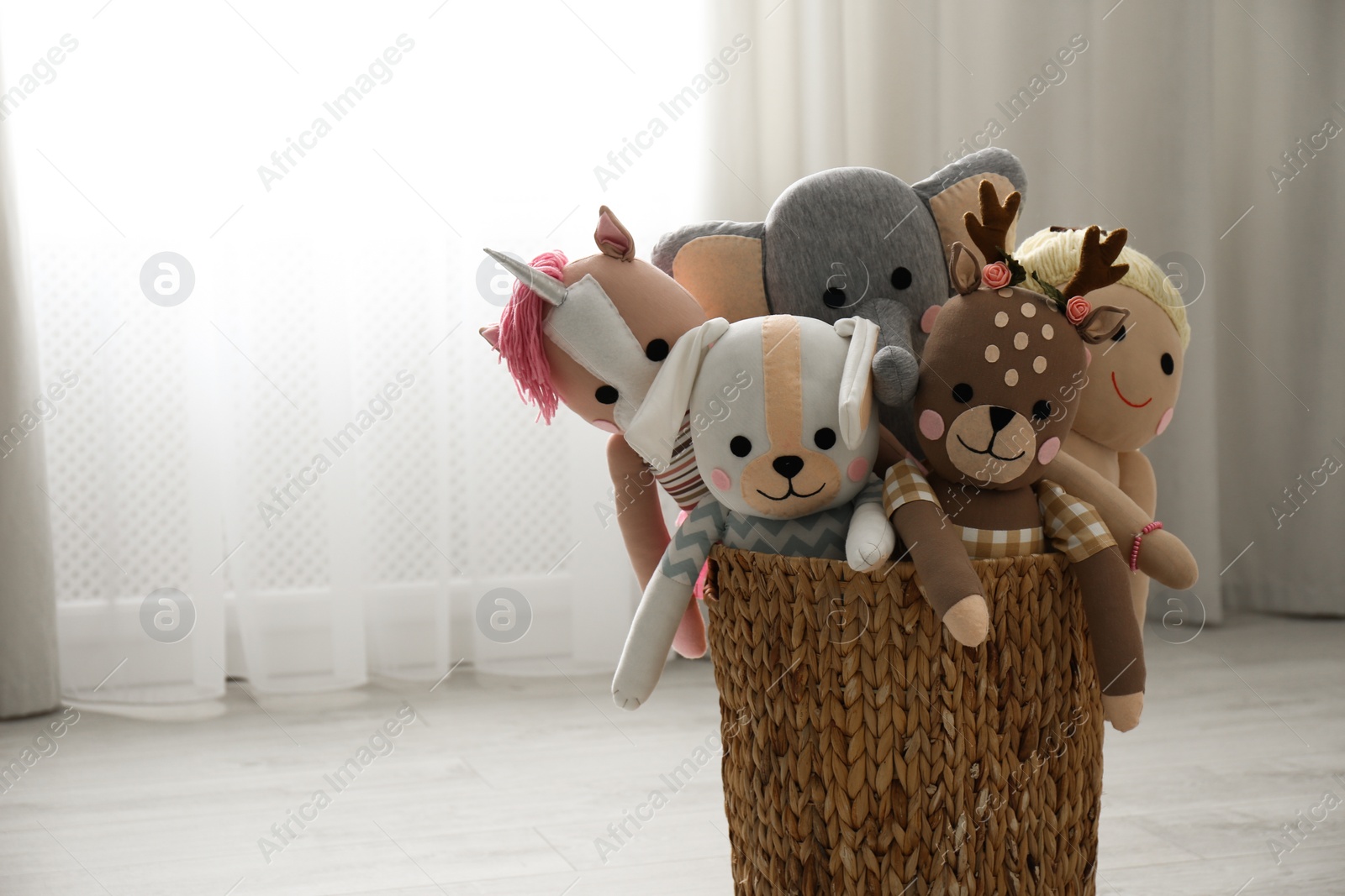 Photo of Funny stuffed toys in basket on floor, space for text. Children's room interior decor