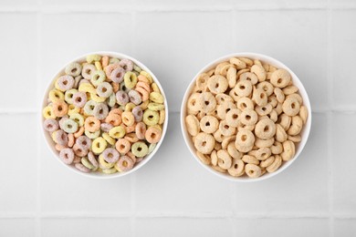 Tasty cereal rings in bowls on white tiled table, flat lay