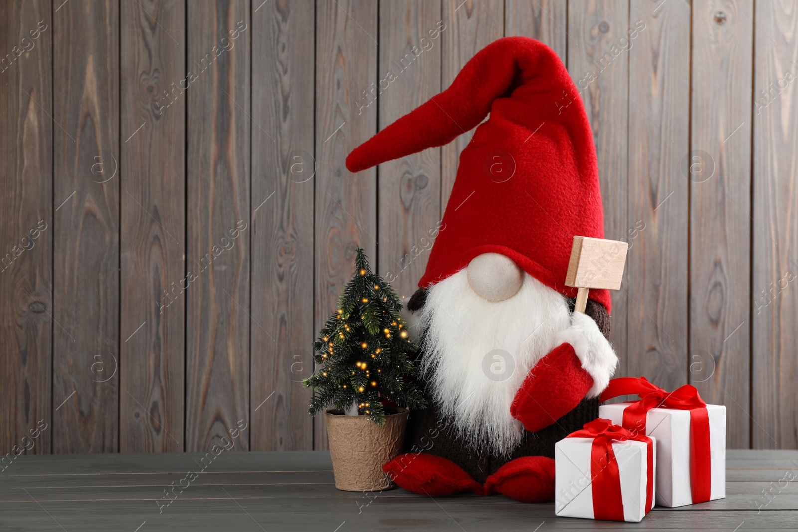 Photo of Cute Christmas gnome, small decorative fir tree and gift boxes on wooden table. Space for text