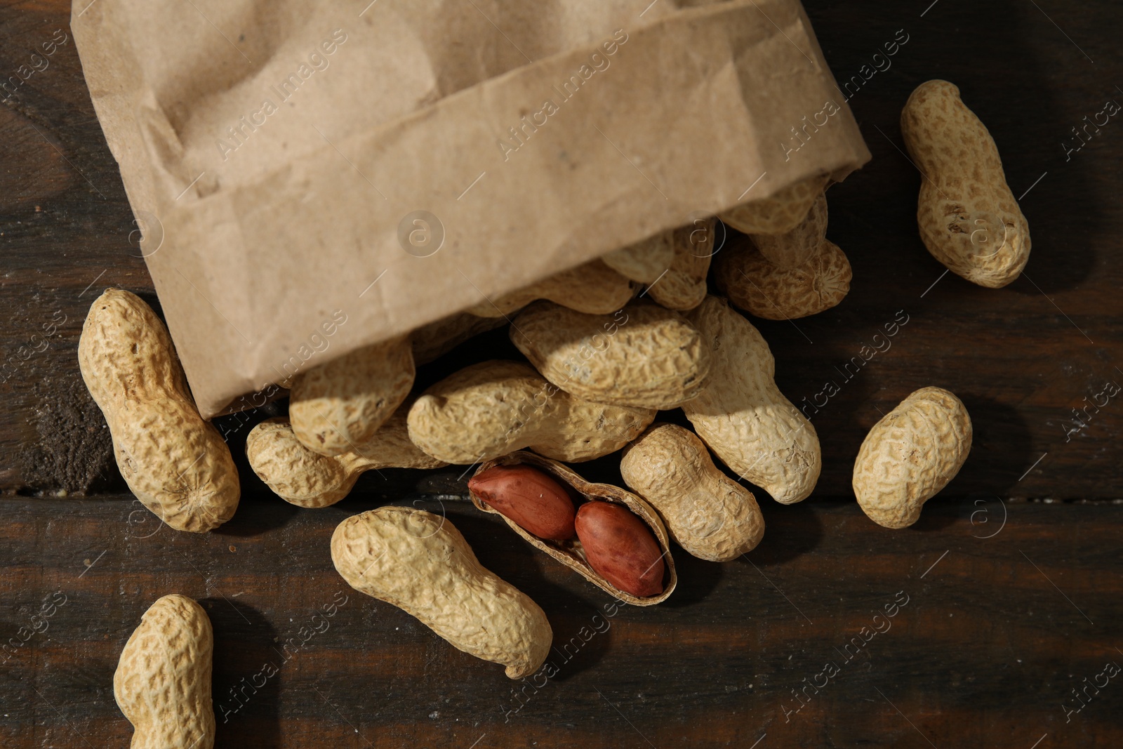 Photo of Paper bag with fresh unpeeled peanuts on wooden table, top view