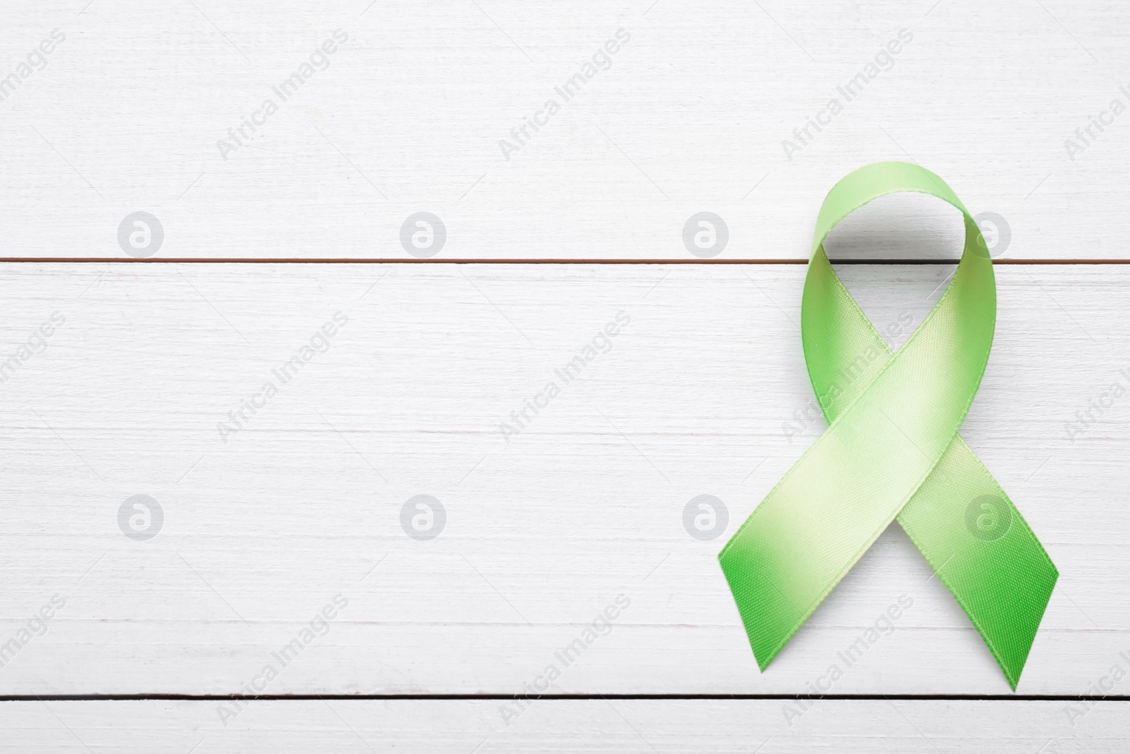 Photo of World Mental Health Day. Green ribbon on white wooden background, top view with space for text