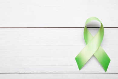 Photo of World Mental Health Day. Green ribbon on white wooden background, top view with space for text