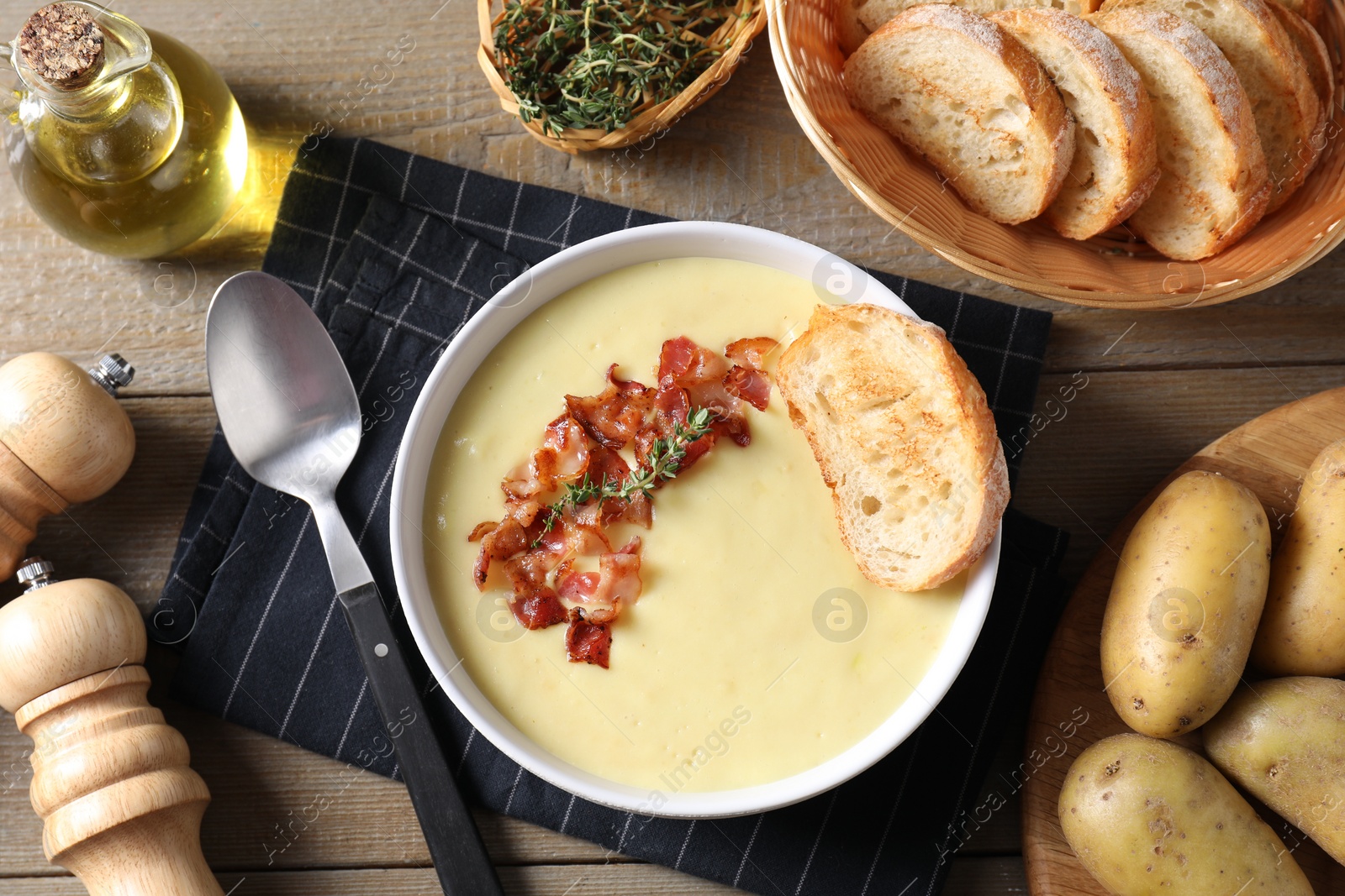 Photo of Tasty potato soup with bacon in bowl served on wooden table, flat lay