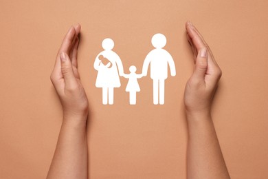 Image of Woman holding hands around paper silhouette of family on coral background, top view. Insurance concept