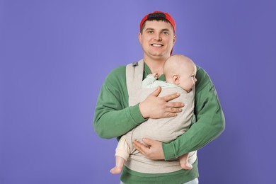 Photo of Father holding his child in sling (baby carrier) on purple background. Space for text