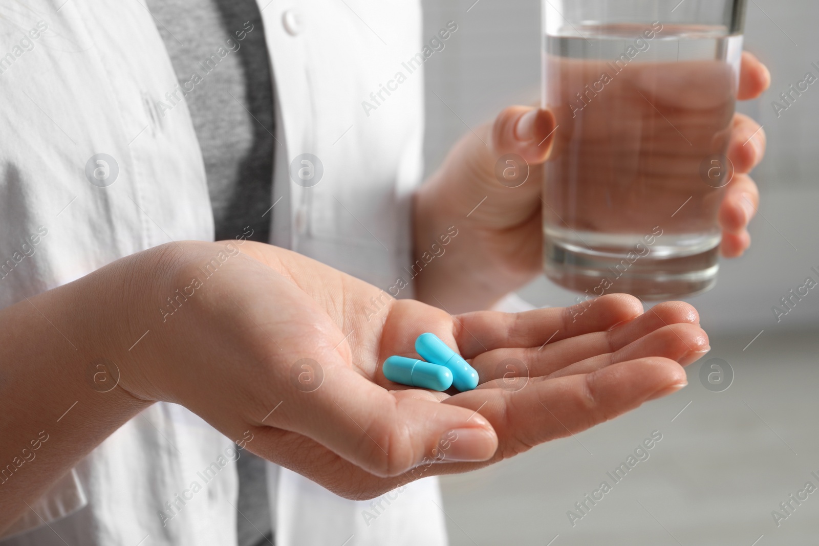 Photo of Woman with glass of water and pills on blurred background, closeup