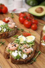 Delicious sandwiches with guacamole, shrimps and microgreens on table, closeup