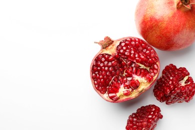 Photo of Whole and cut fresh pomegranates on white background, top view. Space for text