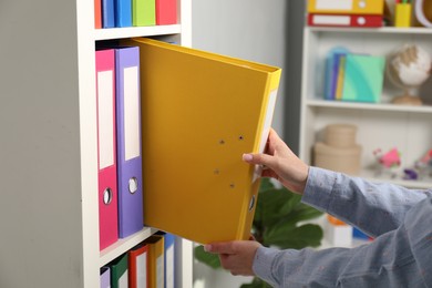 Photo of Woman taking binder office folder from shelving unit indoors, closeup