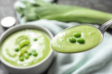 Spoon with fresh vegetable detox soup made of green peas on blurred background, closeup