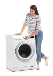 Young woman standing near washing machine with dirty laundry on white background