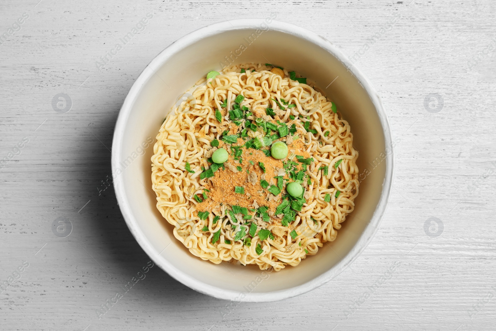 Photo of Cup of instant noodles on white wooden background, top view