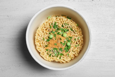 Photo of Cup of instant noodles on white wooden background, top view