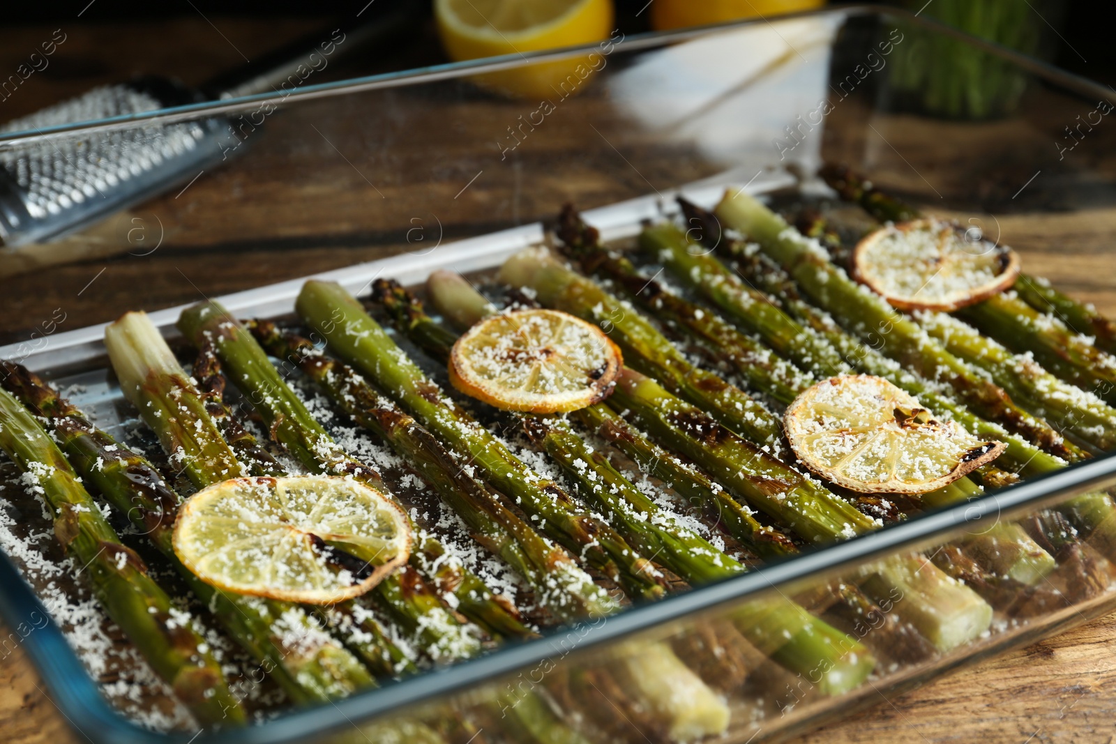 Photo of Oven baked asparagus with lemon slices in glass dish on table, closeup