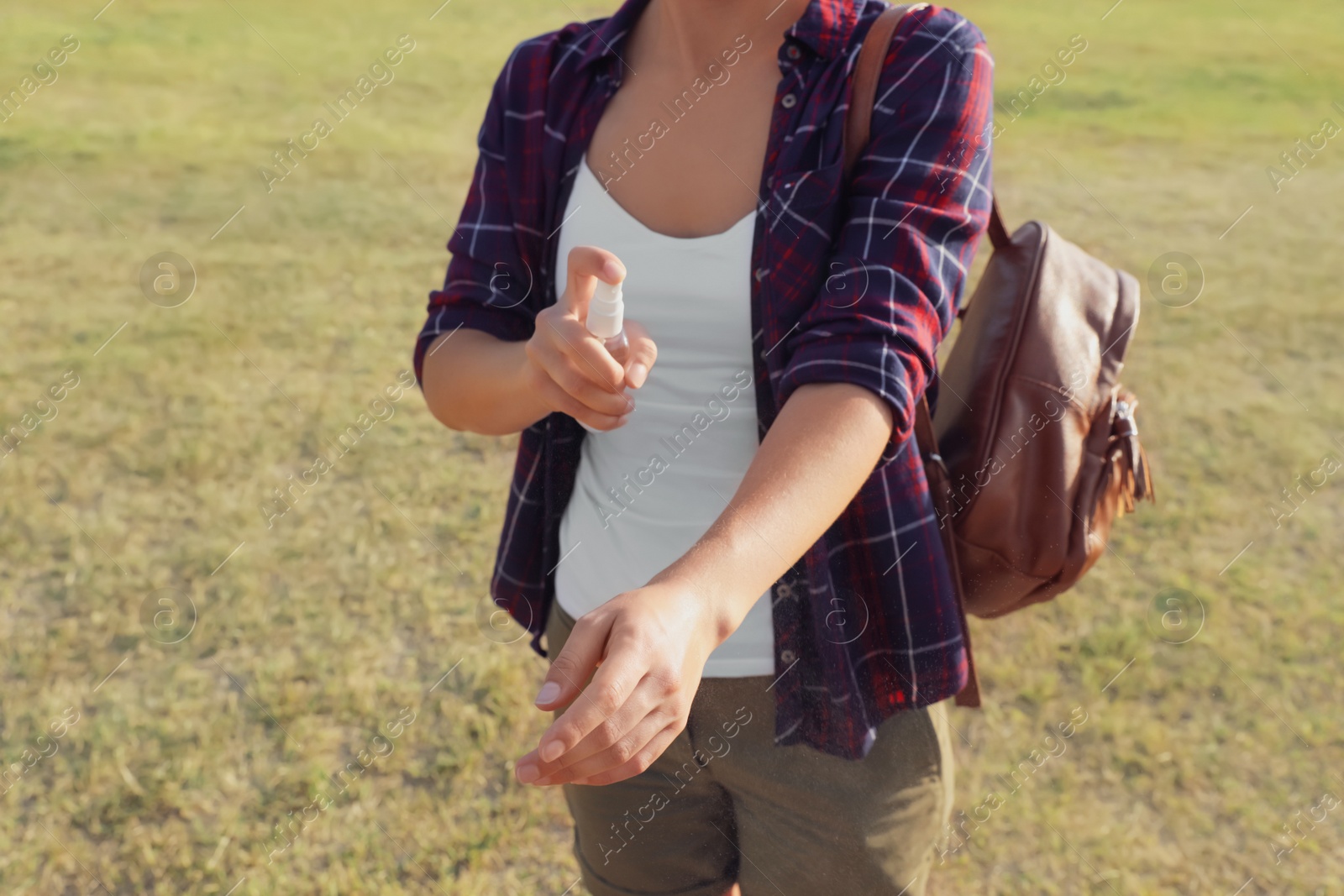 Photo of Woman applying insect repellent onto arm outdoors, closeup