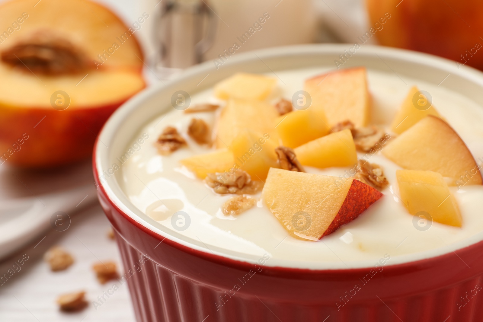 Photo of Delicious yogurt with fresh peach and granola in bowl on table, closeup