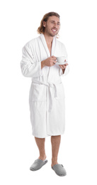 Young man in bathrobe with cup of drink on white background