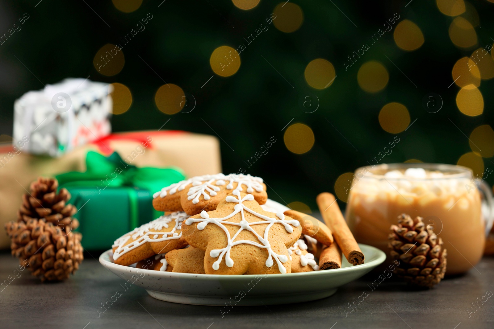 Photo of Decorated cookies and hot drink on grey table against blurred Christmas lights