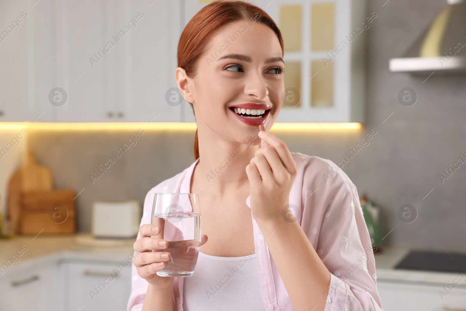 Photo of Beautiful young woman taking vitamin pill at home