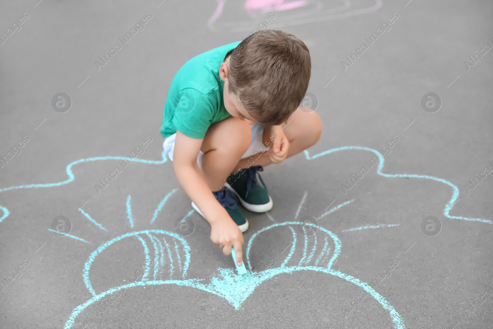 Photo of Little child drawing with chalk on asphalt