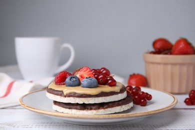 Photo of Crunchy rice cakes with peanut butter and sweet berries served on white wooden table, closeup