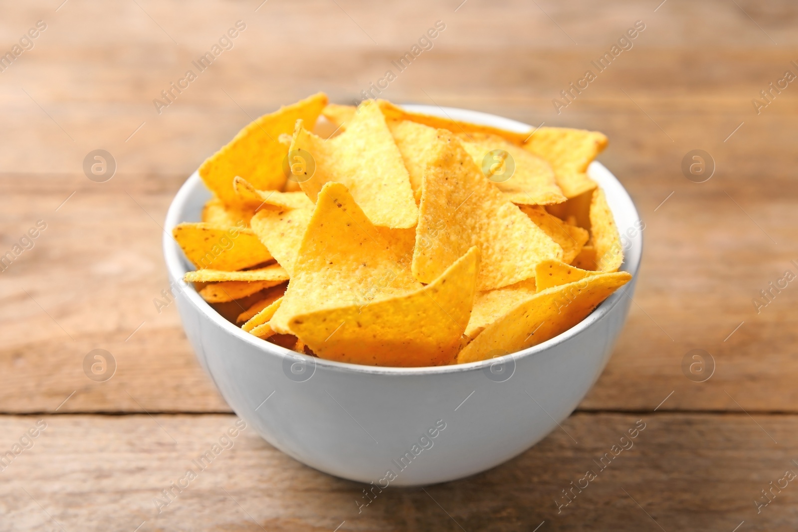 Photo of Tasty mexican nachos chips in bowl on wooden table