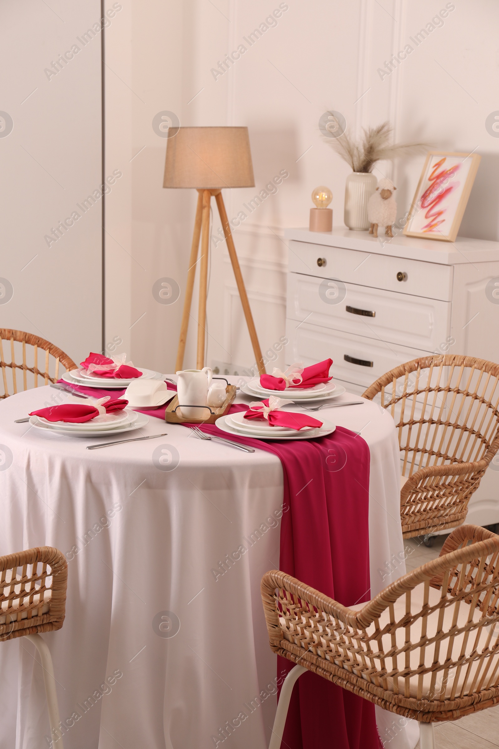 Photo of Color accent table setting. Plates, cutlery and pink napkins in dining room