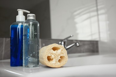 Natural loofah sponge and shower gel bottles on washbasin in bathroom. Space for text