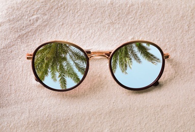 Image of Green palm leaves reflecting in sunglasses on sandy beach, top view