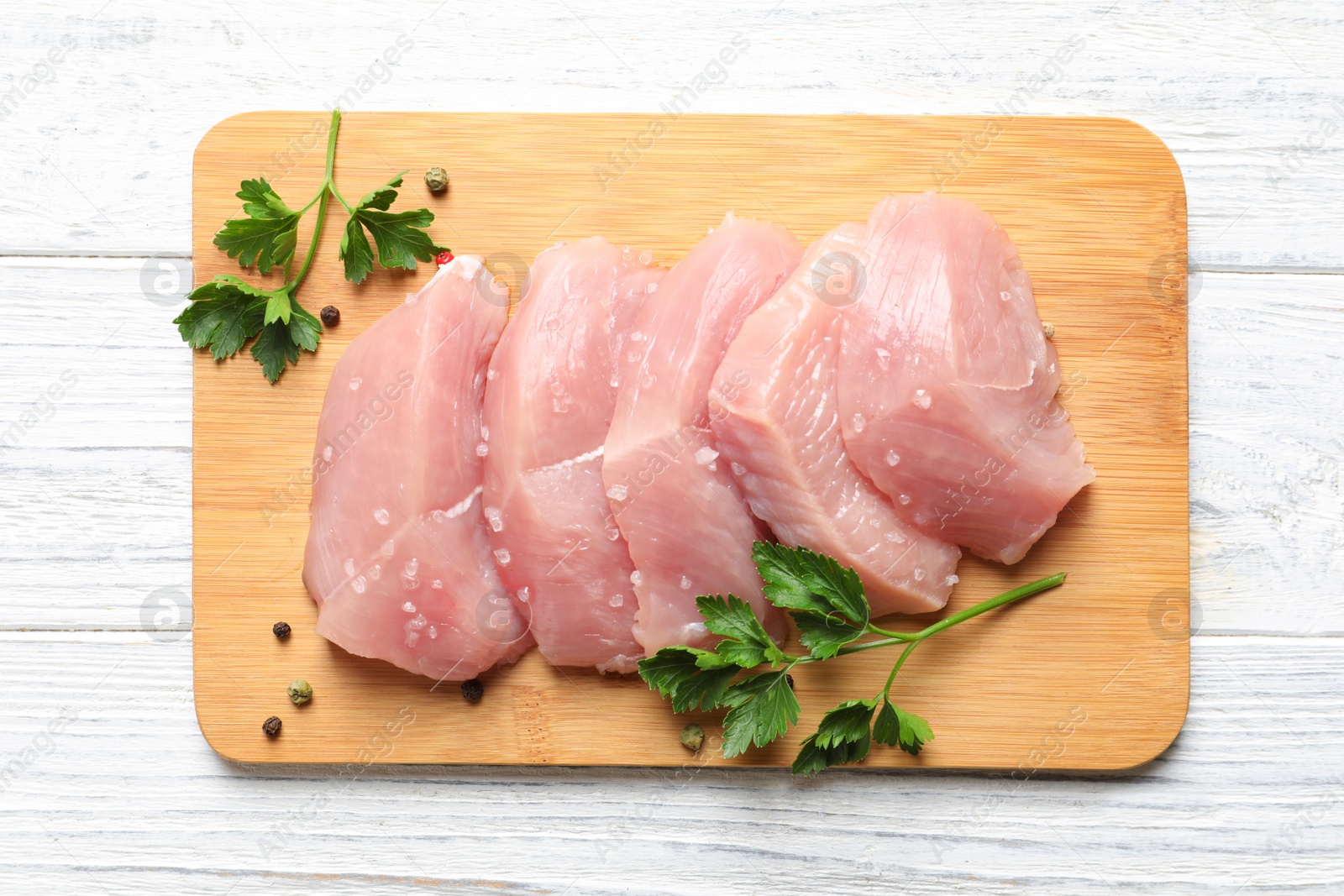 Photo of Board with cut raw turkey fillet and parsley on white wooden background, top view